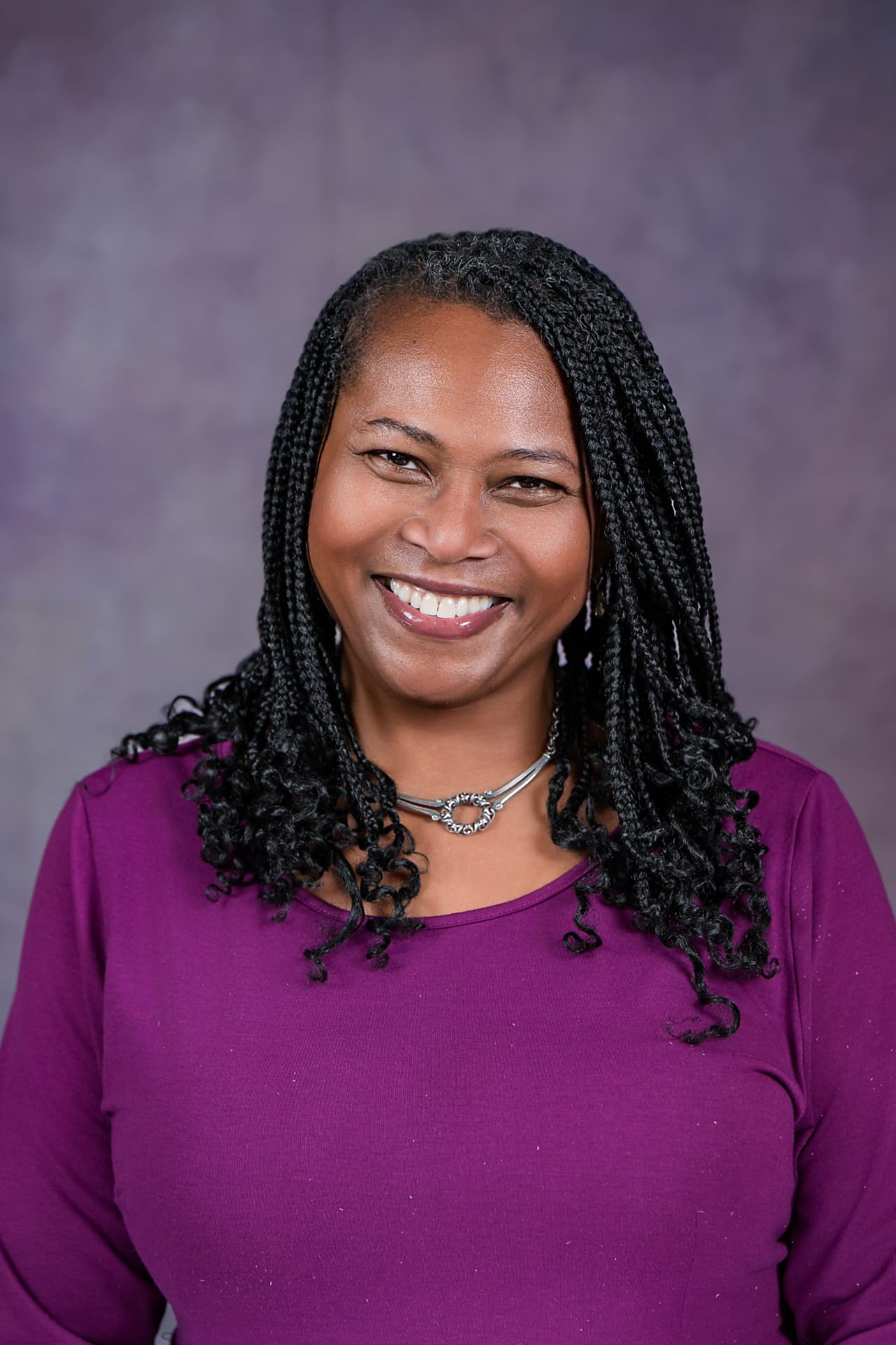 Studio headshot of a smiling woman with braids in a magenta top