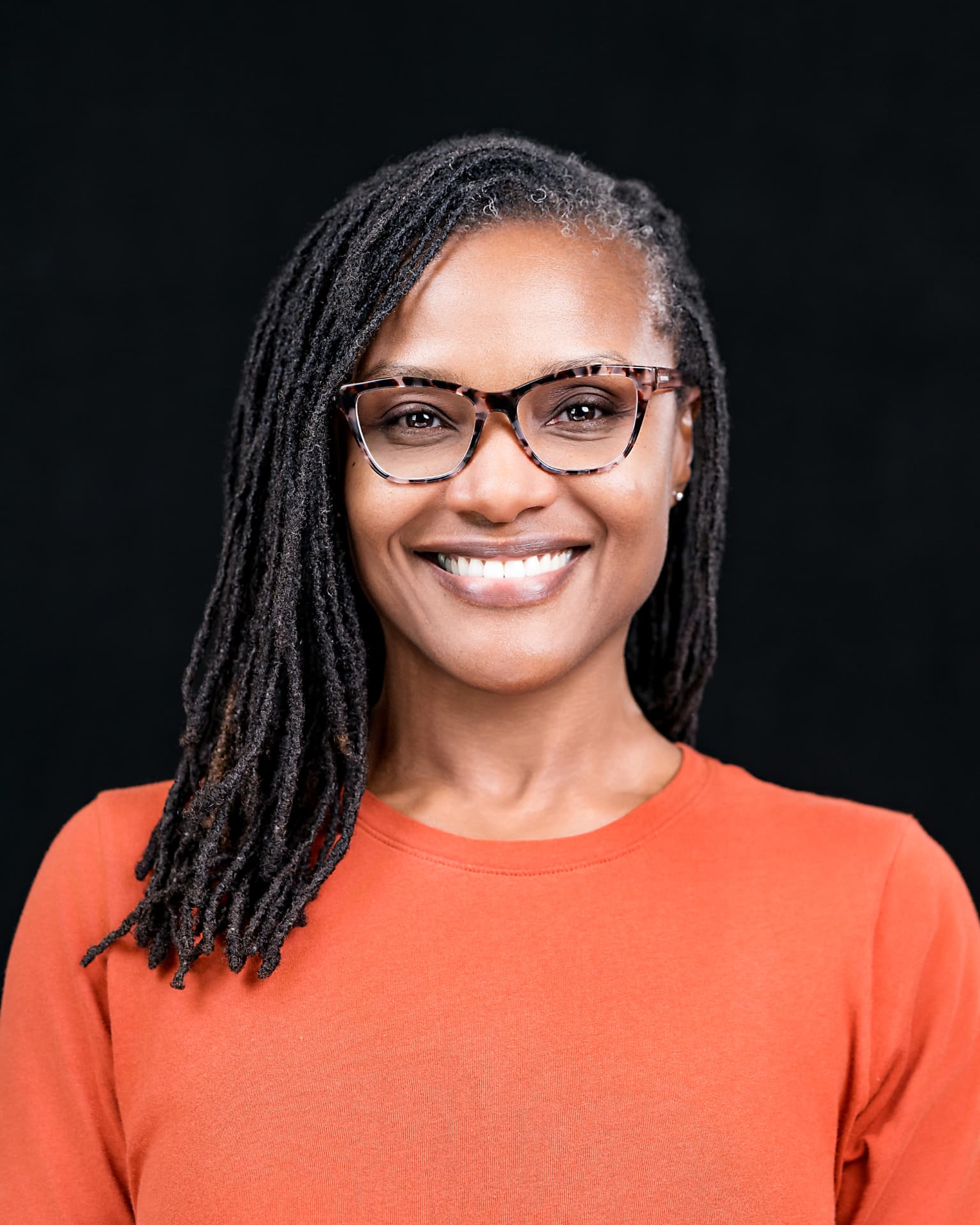 Studio headshot of a professional woman in an orange top on a black backdrop
