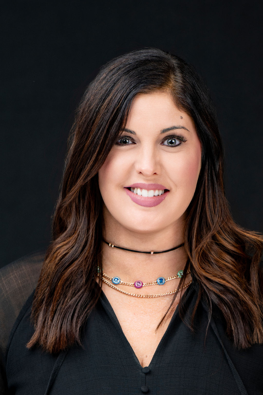 Studio headshot of a smiling woman with long dark hair in a black blouse