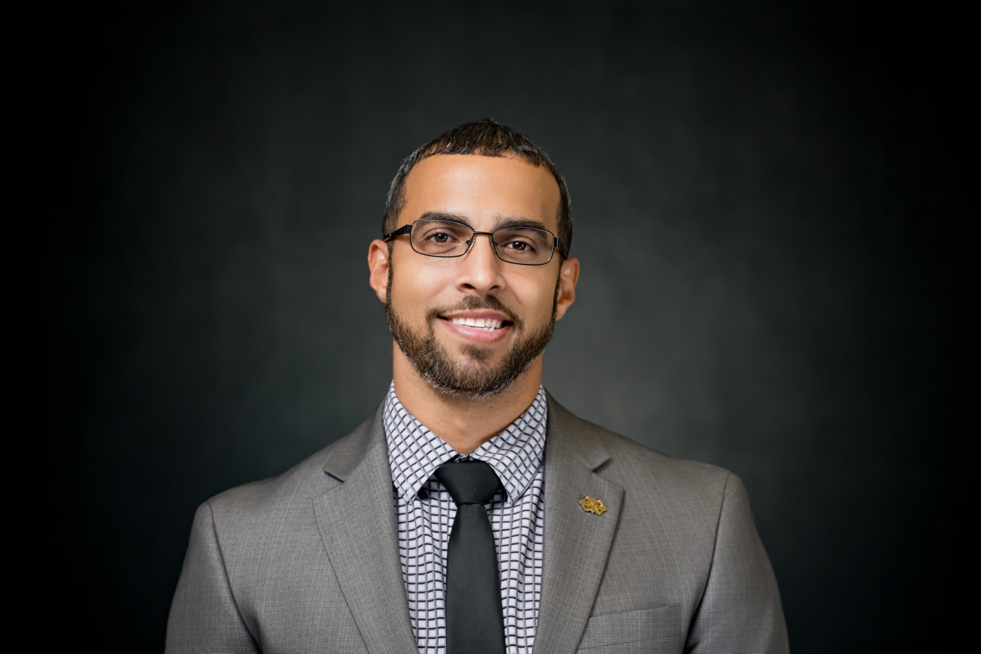 Studio headshot of a smiling man in a grey suit and black tie