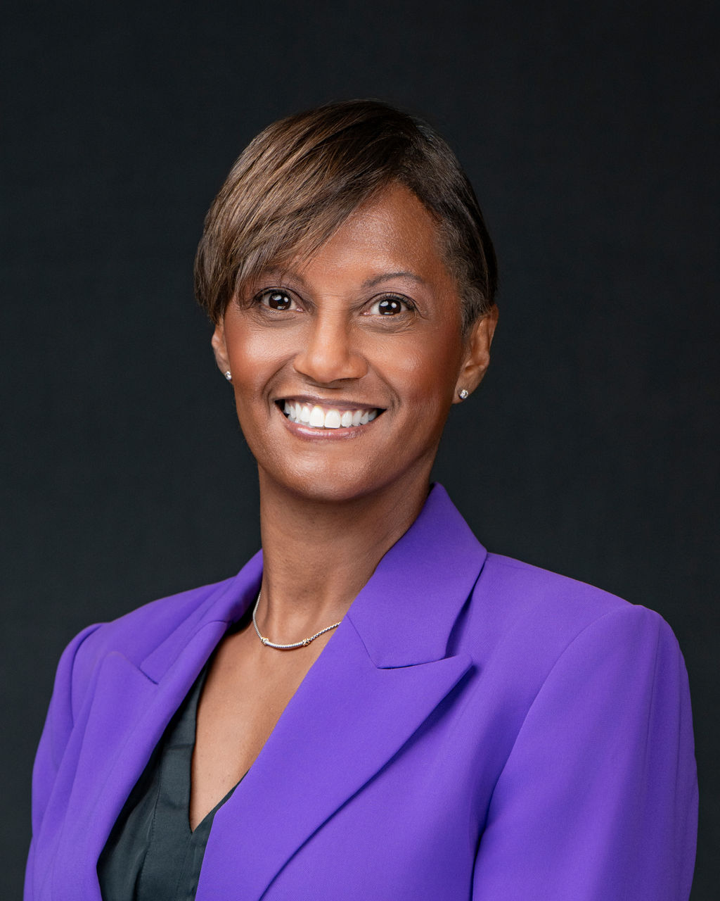 Studio headshot of a smiling woman with short hair in a purple blazer