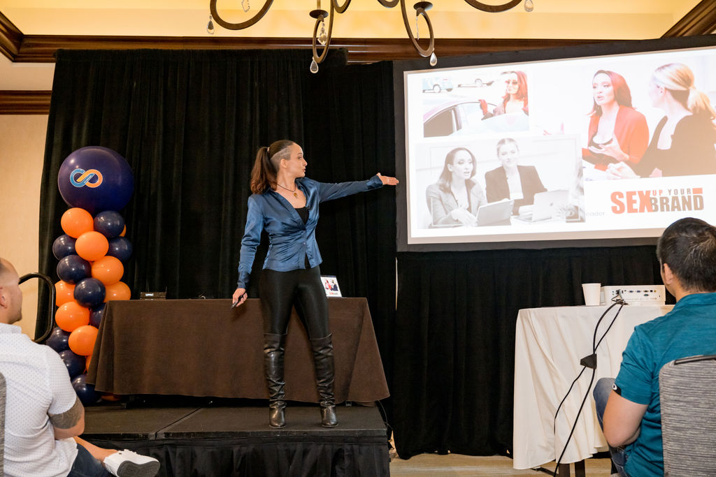 Presenter on a breakout stage beside orange and navy balloons at Limitless Expo
