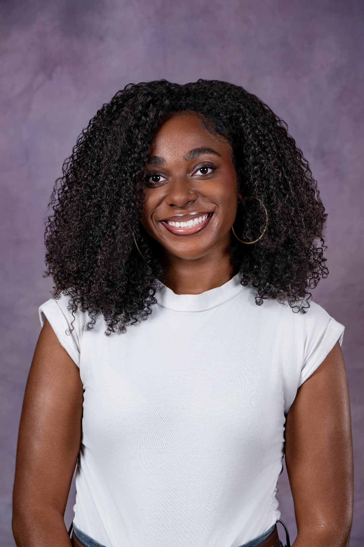 Studio headshot of a smiling woman with curly hair in a white top