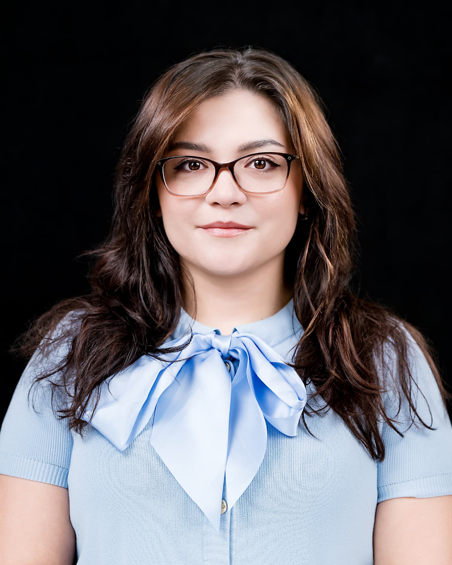 Studio headshot of a professional woman in a light blue bow-tie top