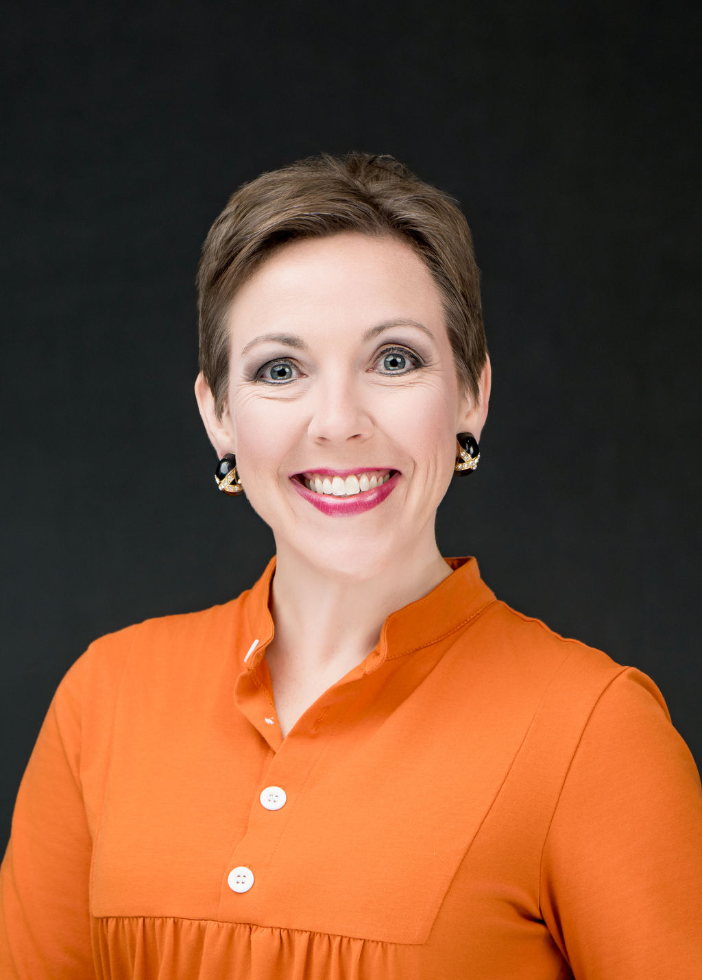 Studio headshot of a smiling woman with short hair in an orange blouse