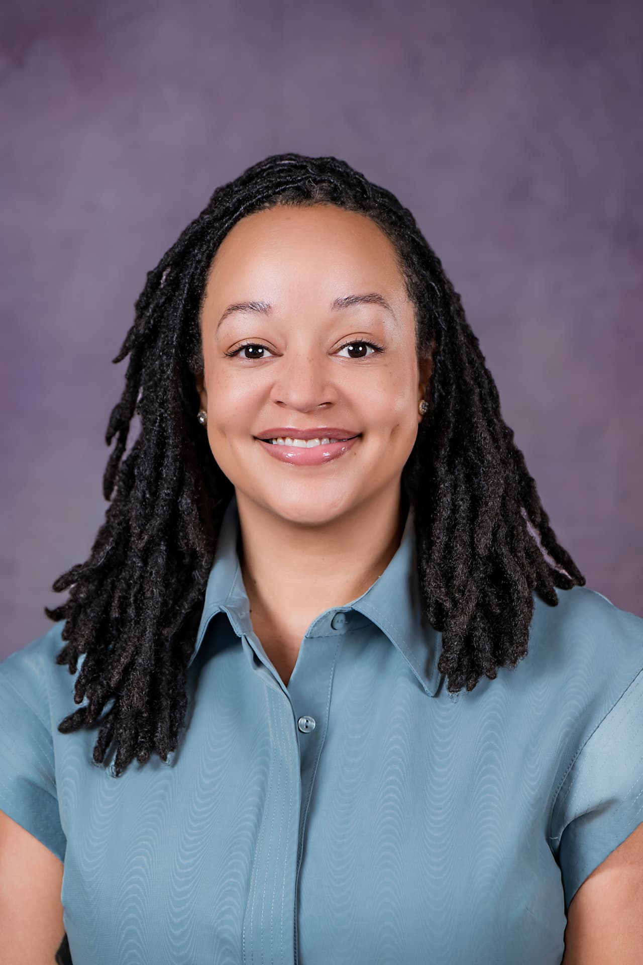 Studio headshot of a professional woman in a blue shirt on a purple backdrop