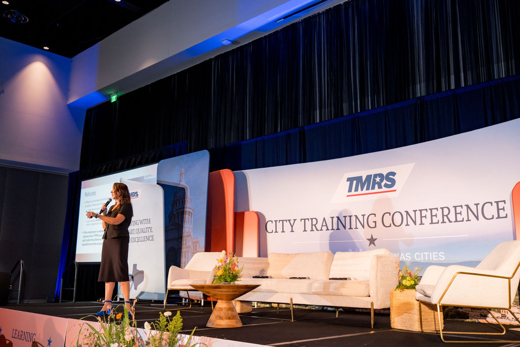 Wide stage view of a TMRS presentation with lounge seating and conference backdrop