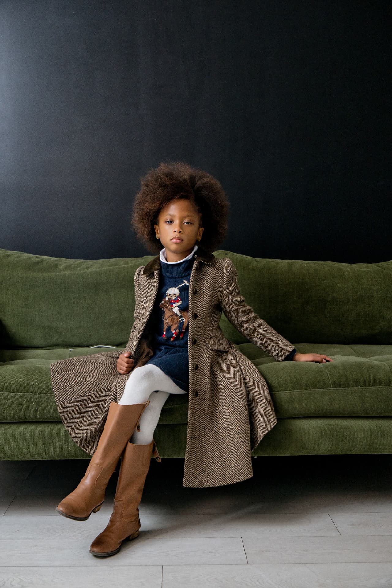 Young model in a herringbone coat seated on a green velvet sofa for an editorial shoot