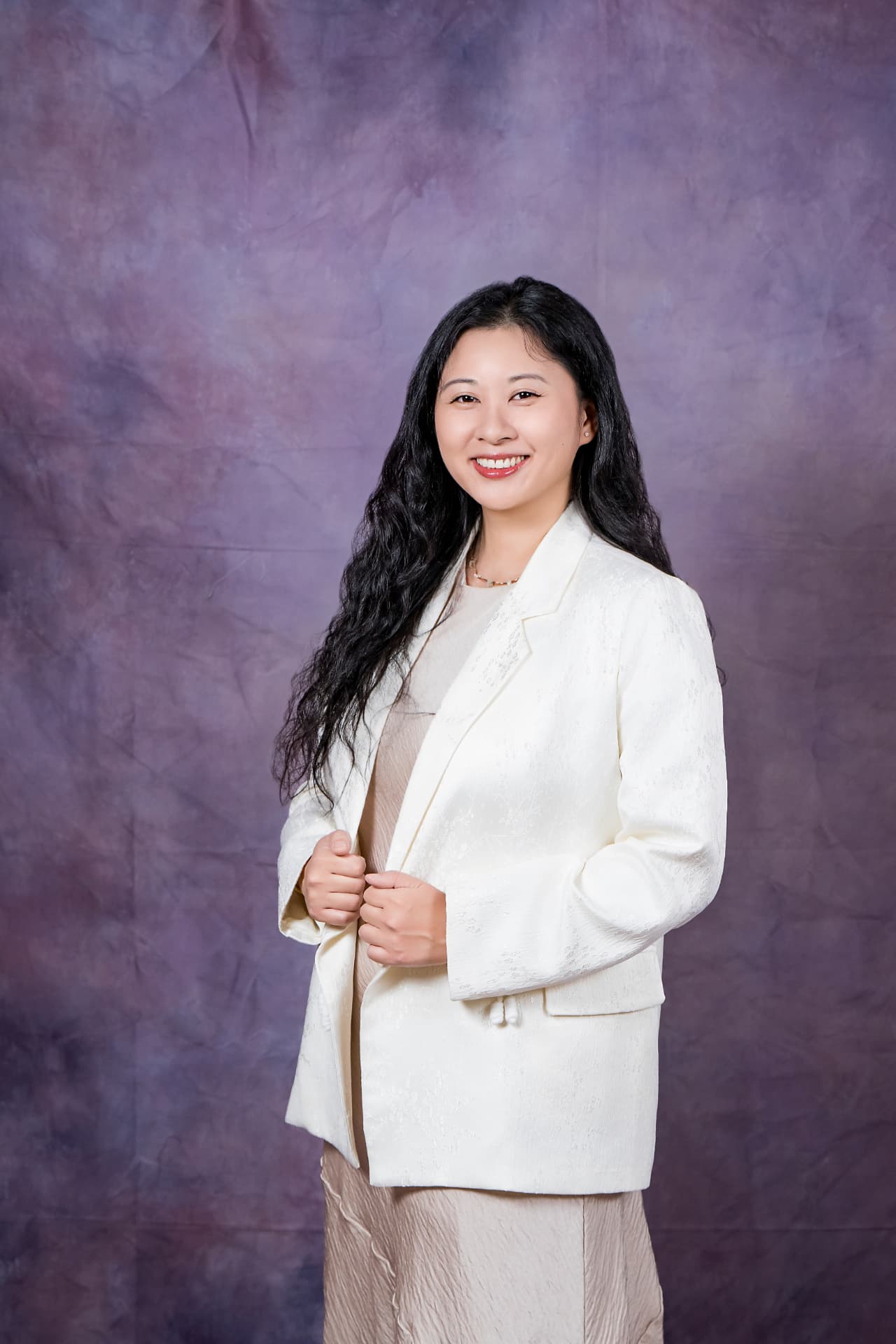 Studio portrait of a smiling woman with long dark hair in a cream jacket
