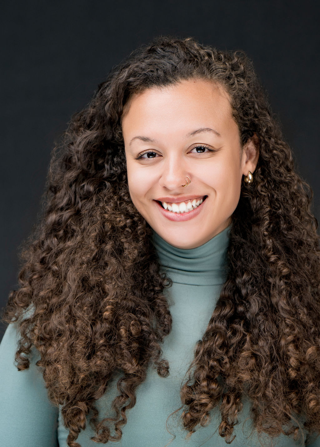 Studio headshot of a smiling woman with long curly hair in a sage turtleneck