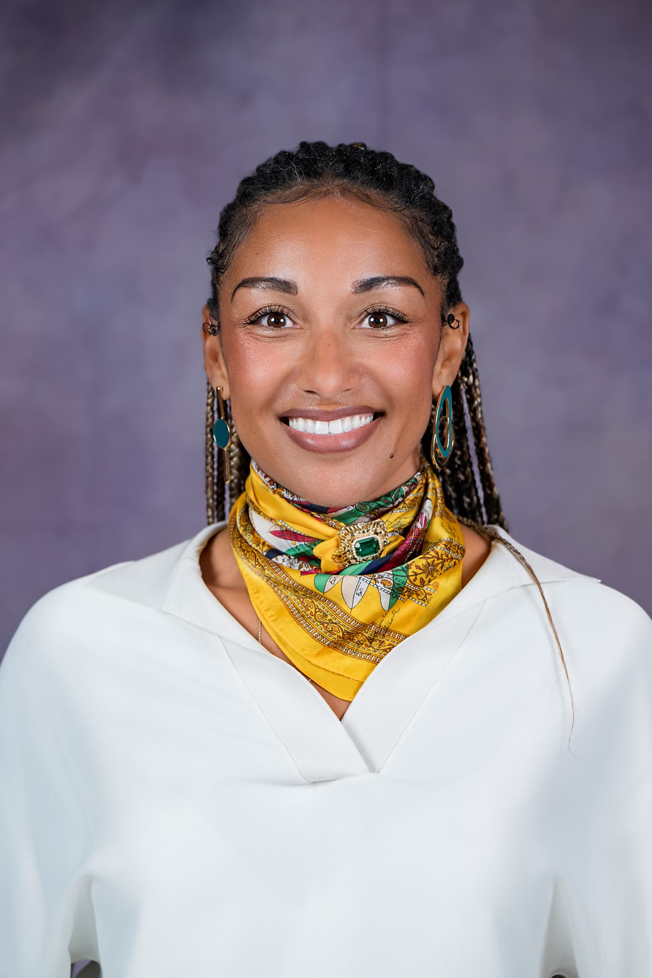 Studio headshot of a smiling woman in a white top and yellow scarf