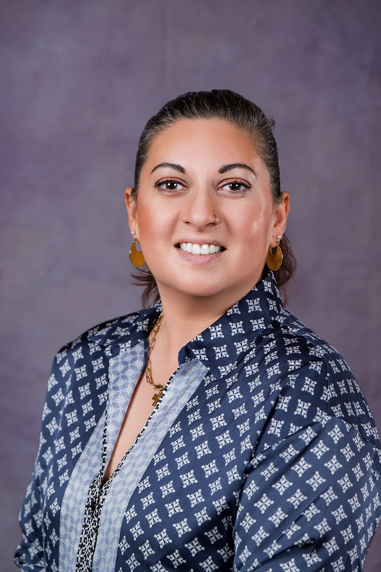Studio headshot of a smiling woman in a patterned blue blouse