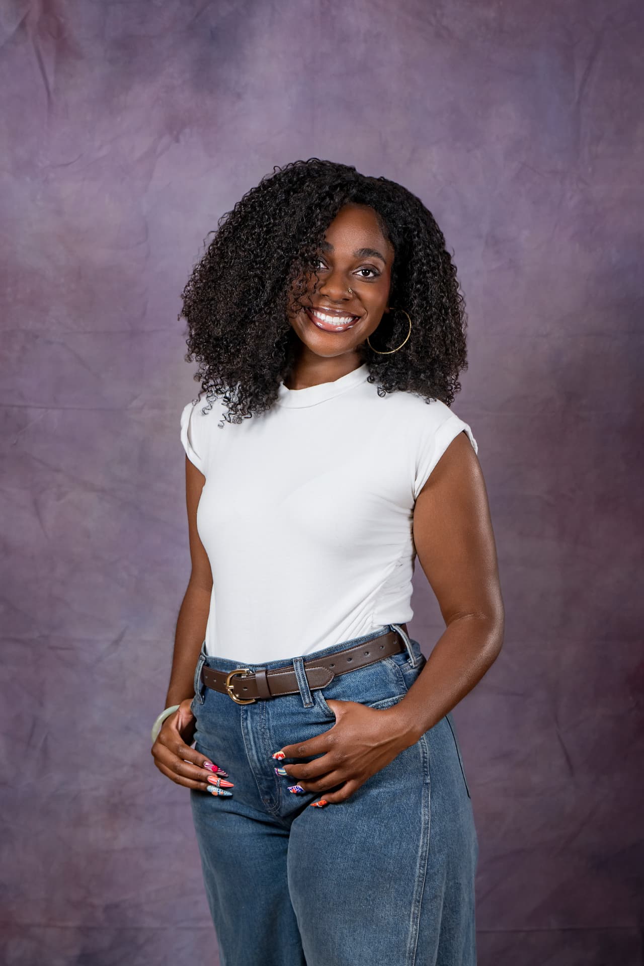 Studio portrait of a smiling woman with curly hair in a white top and jeans