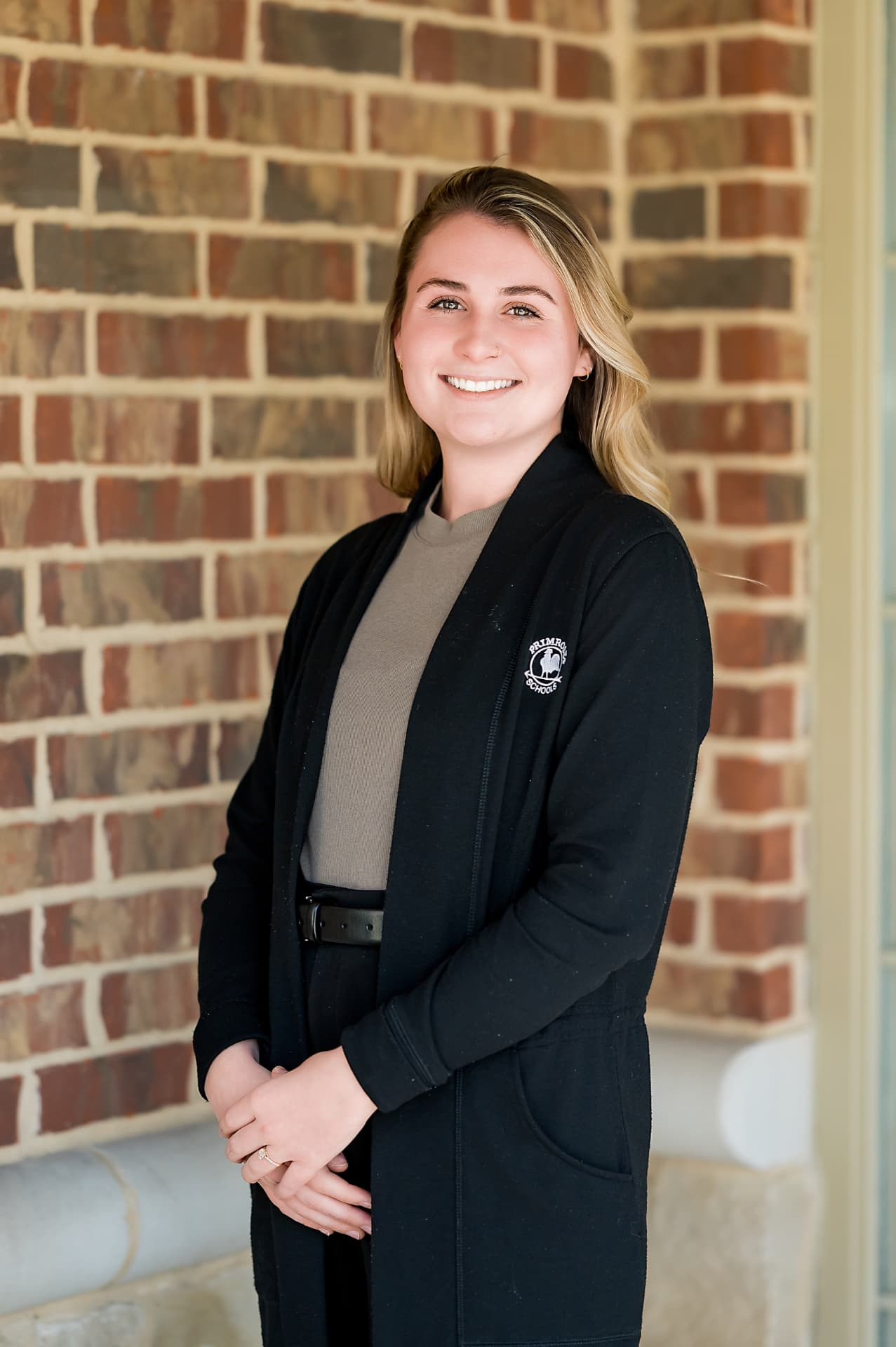 Staff portrait of a woman in a branded black cardigan against a brick wall