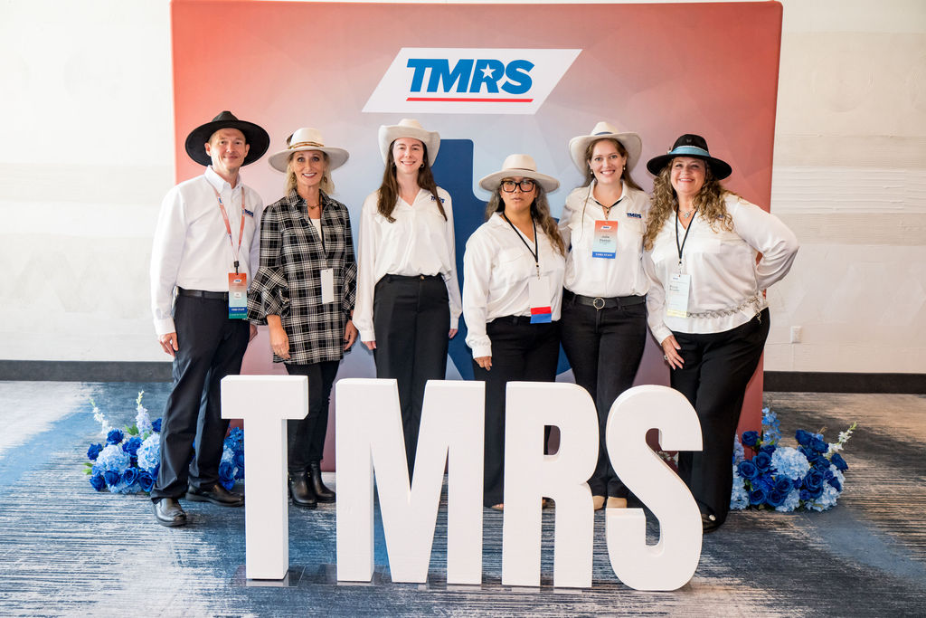 TMRS staff team posing in hats behind large TMRS letters