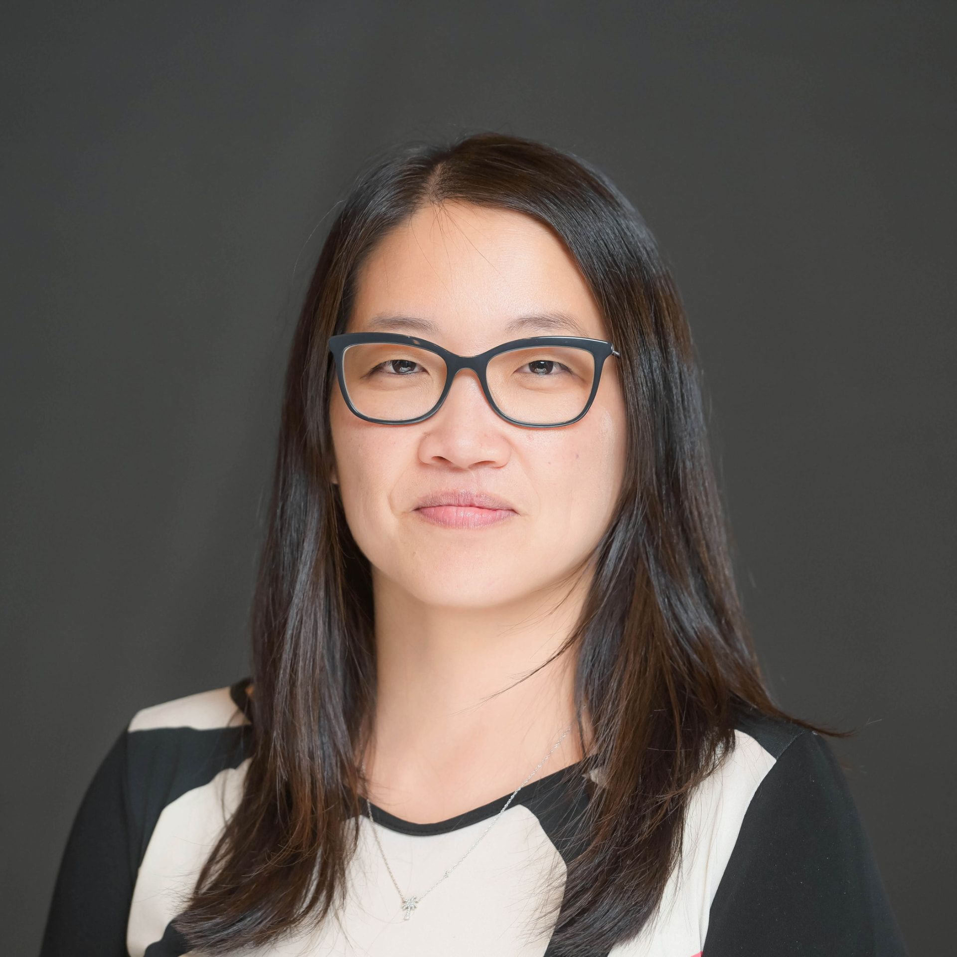 Studio headshot of a professional woman with glasses on a grey backdrop