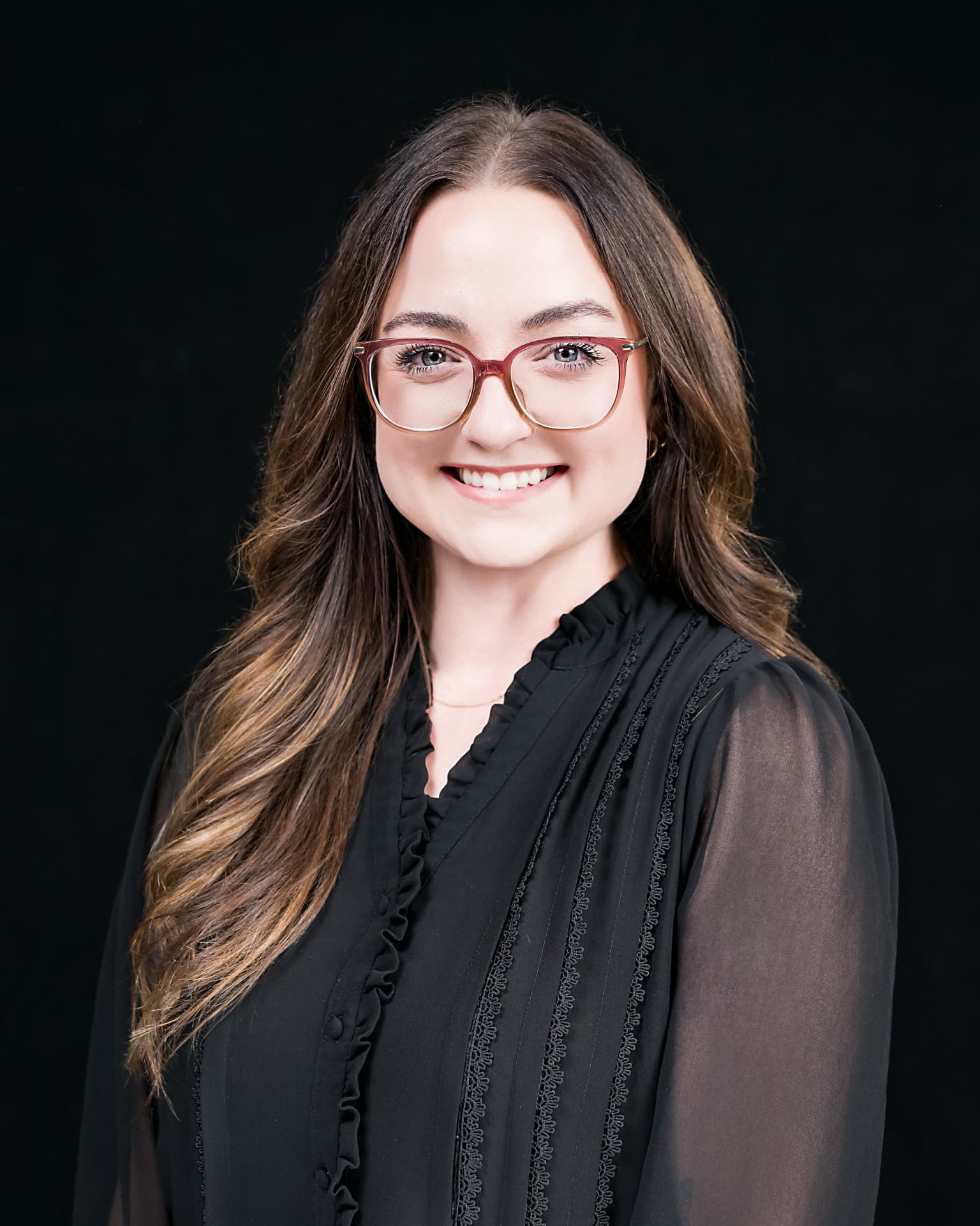 Studio headshot of a professional woman with glasses in a black blouse