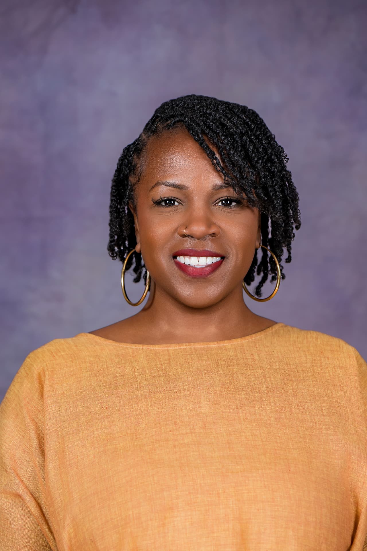 Studio headshot of a smiling woman in a golden yellow top