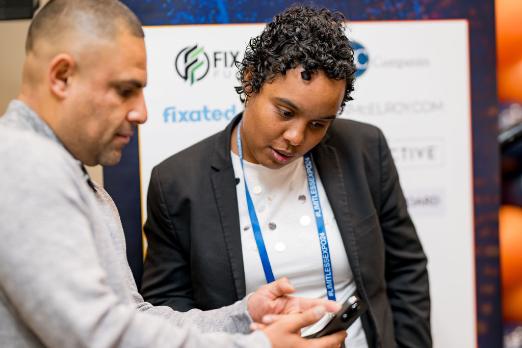 Attendees exchanging contact details at a Limitless Expo sponsor backdrop