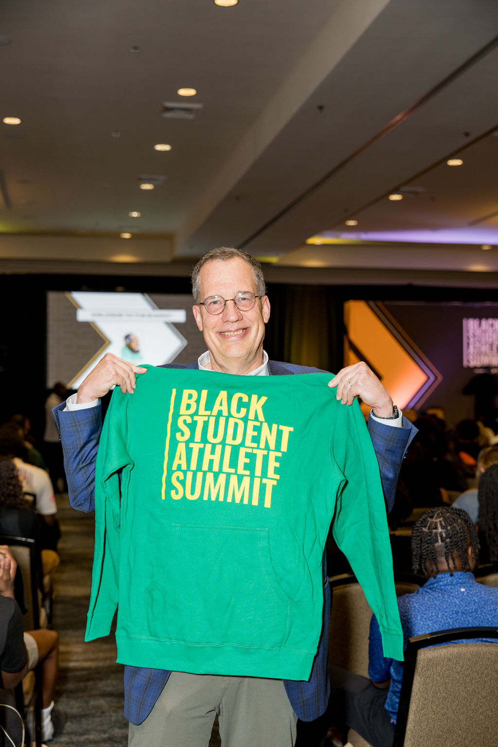 Guest holding up a Black Student Athlete Summit sweatshirt