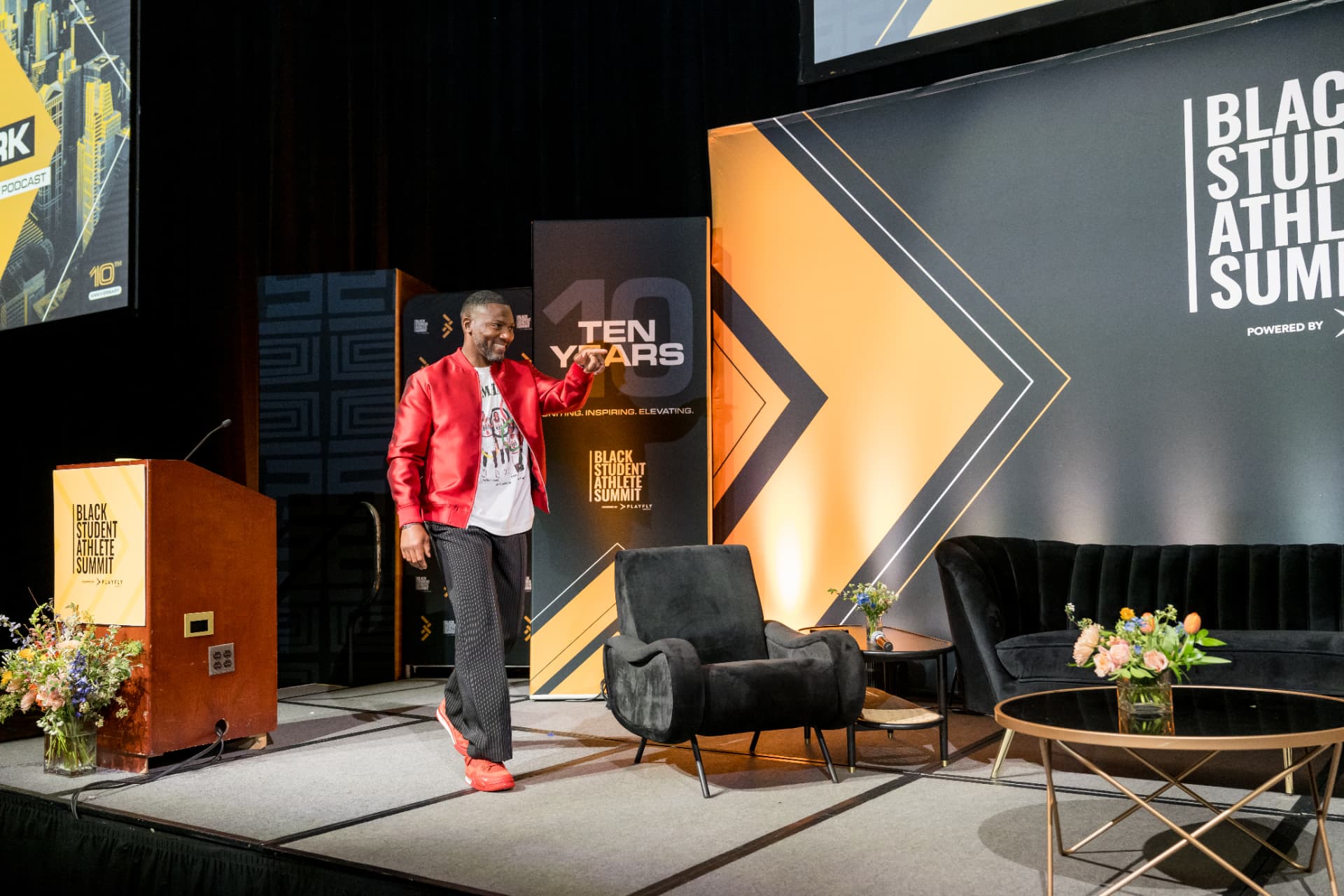 Speaker in a red jacket walking the stage at the Black Student Athlete Summit