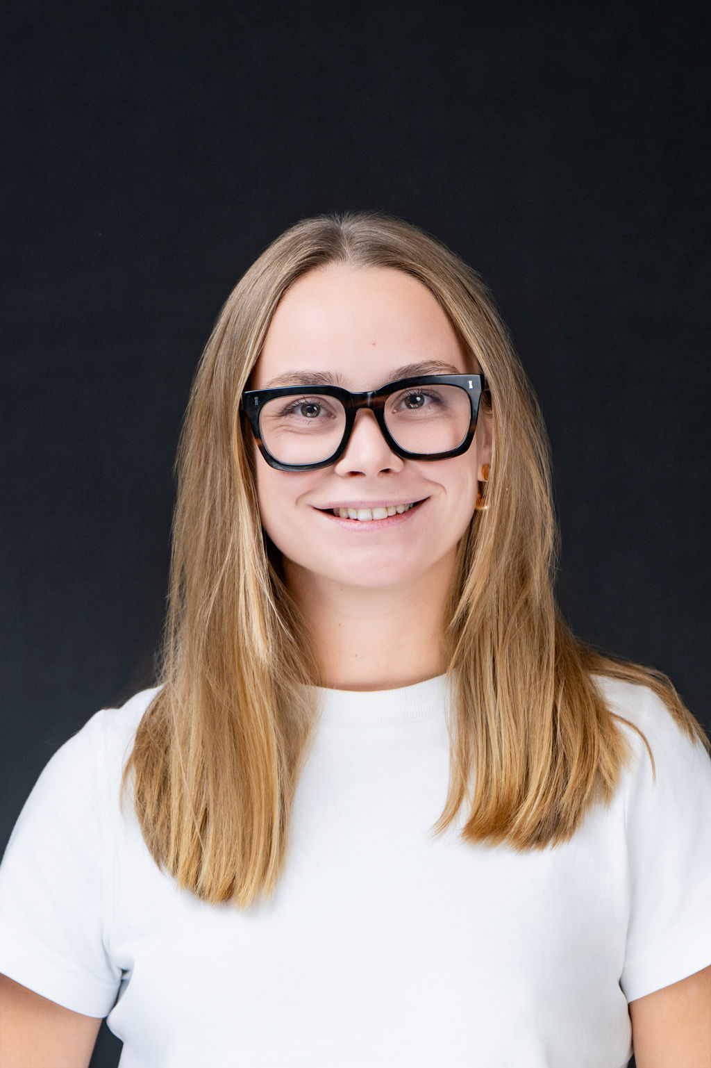 Studio headshot of a smiling woman with glasses in a white tee