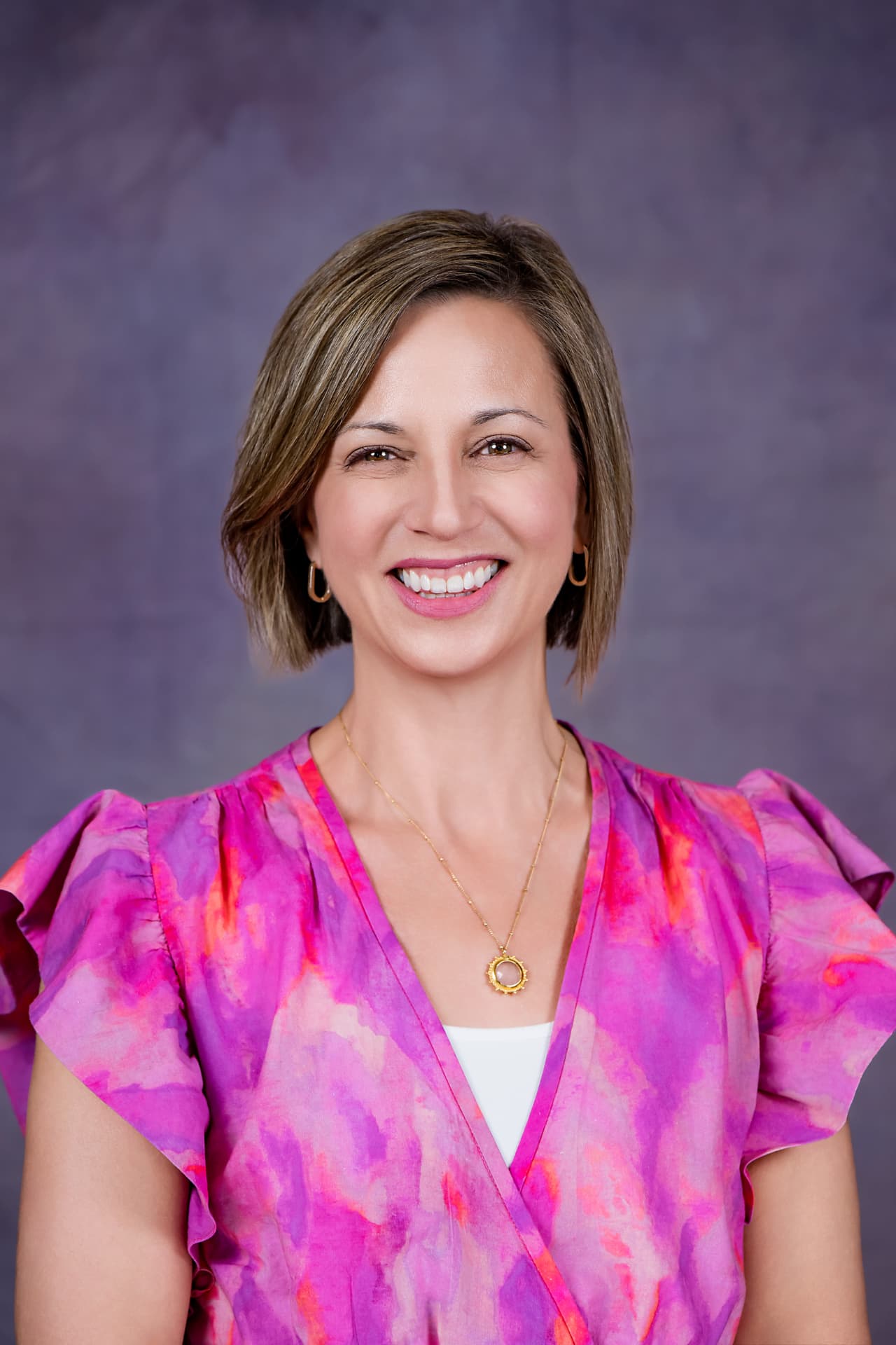 Studio headshot of a smiling woman in a pink floral blouse