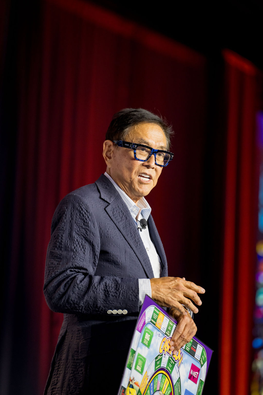Keynote speaker holding a Cashflow board game on stage at Limitless Expo