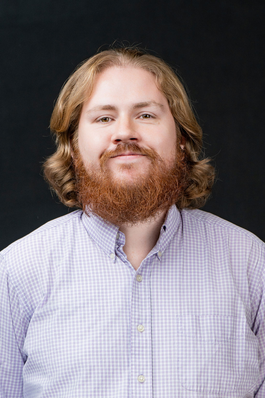 Studio headshot of a man with a red beard in a lavender checked shirt