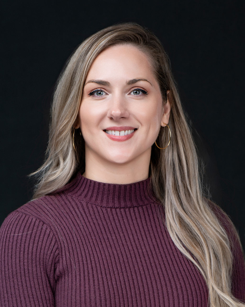 Studio headshot of a smiling woman with blonde hair in a plum turtleneck