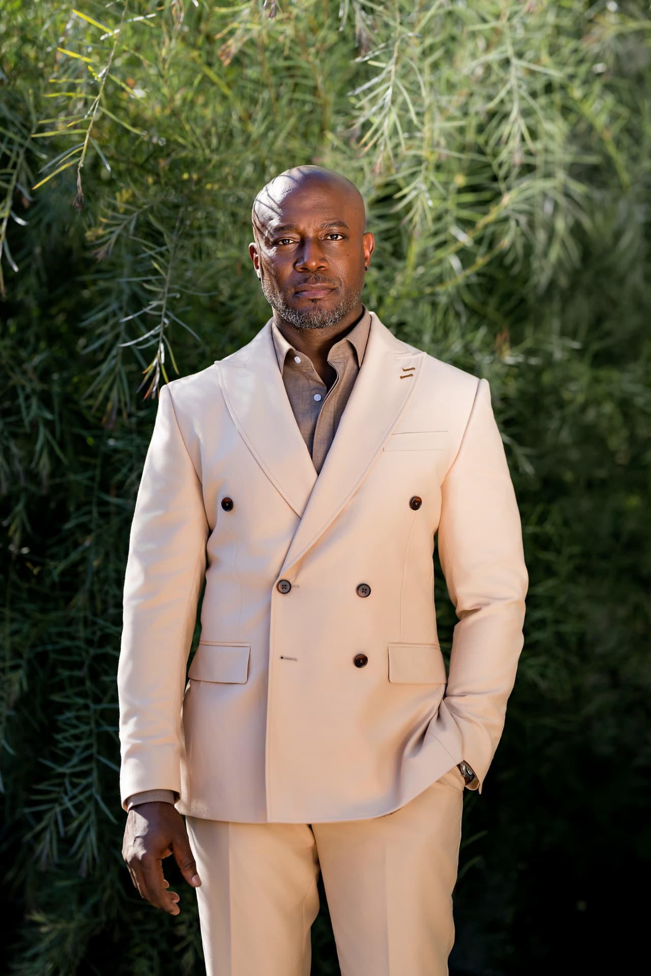 Executive portrait in a cream double-breasted suit against green foliage
