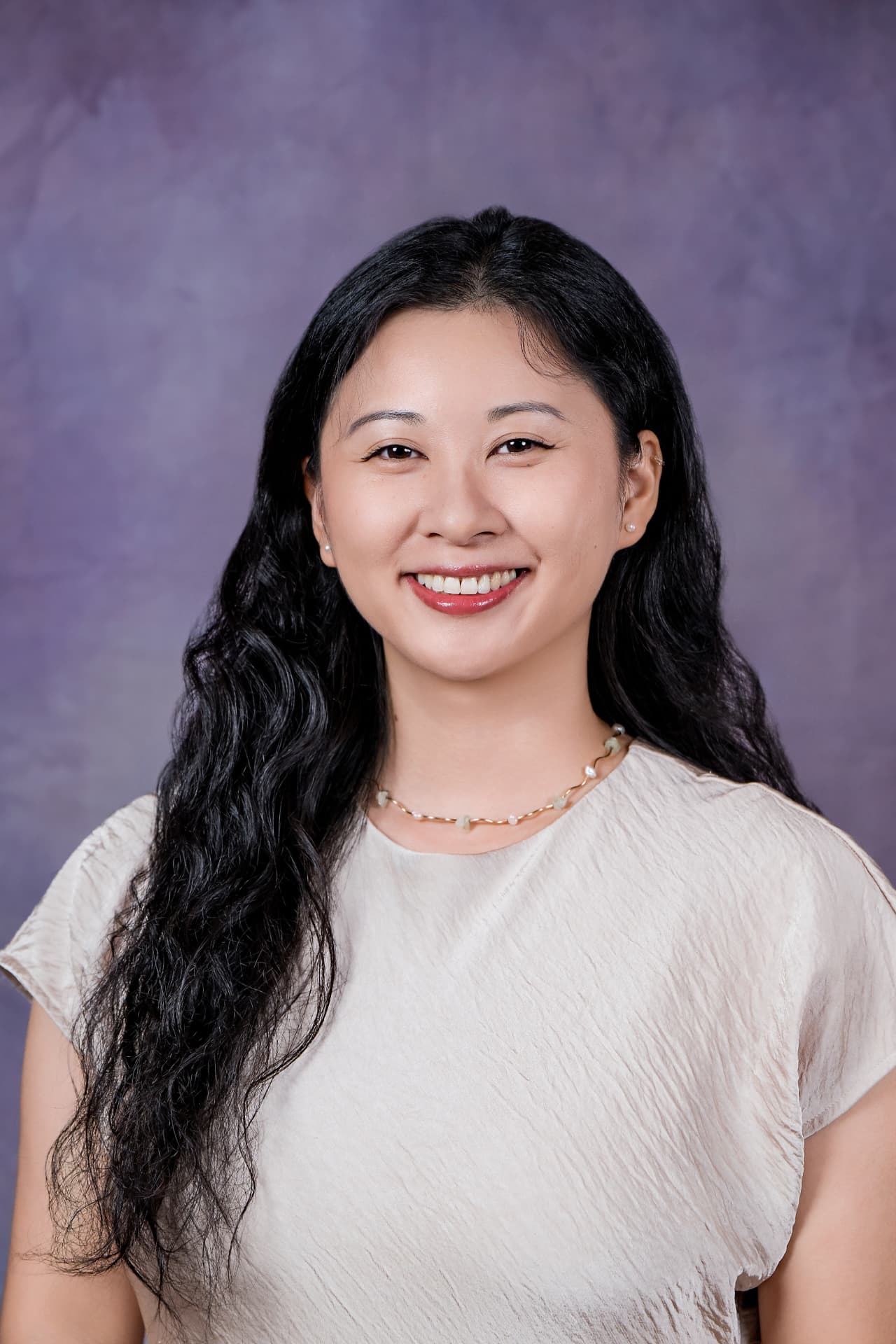 Studio headshot of a smiling woman with long wavy hair in a beige top