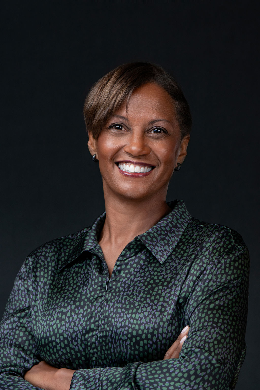 Studio headshot of a smiling woman with arms crossed in a green patterned blouse