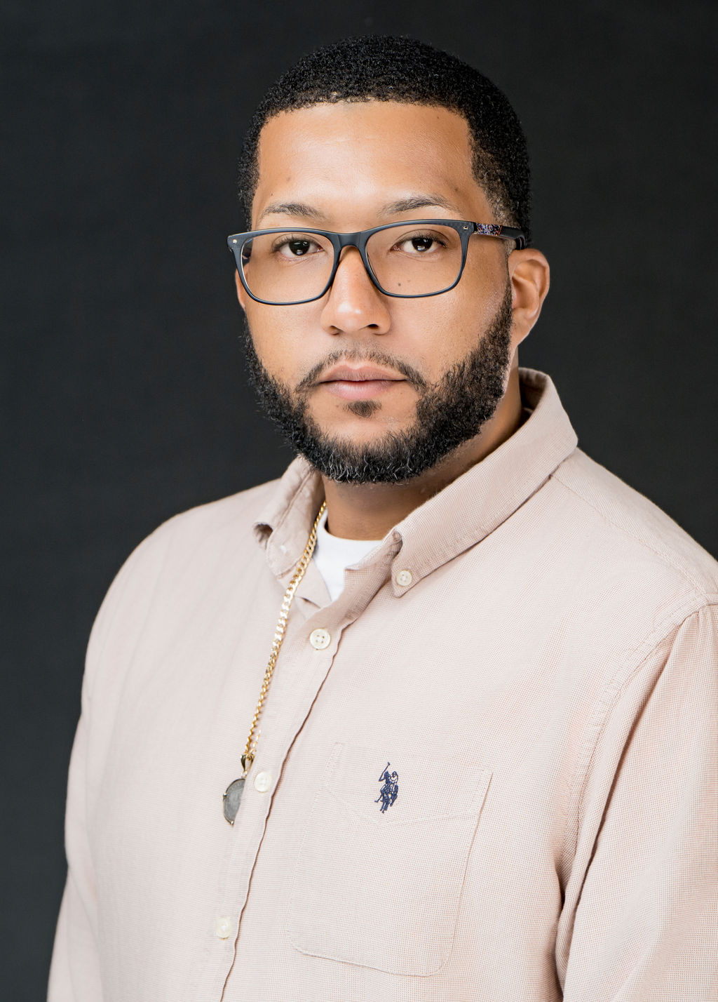 Studio headshot of a man in glasses and a tan button-down shirt