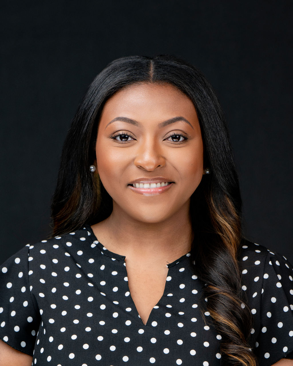 Studio headshot of a smiling woman in a black-and-white polka dot blouse