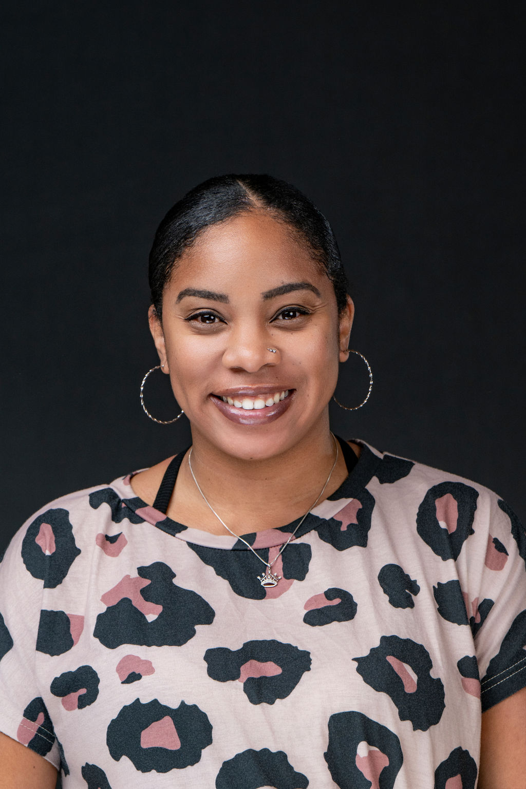 Studio headshot of a smiling woman with hoop earrings in a leopard print top
