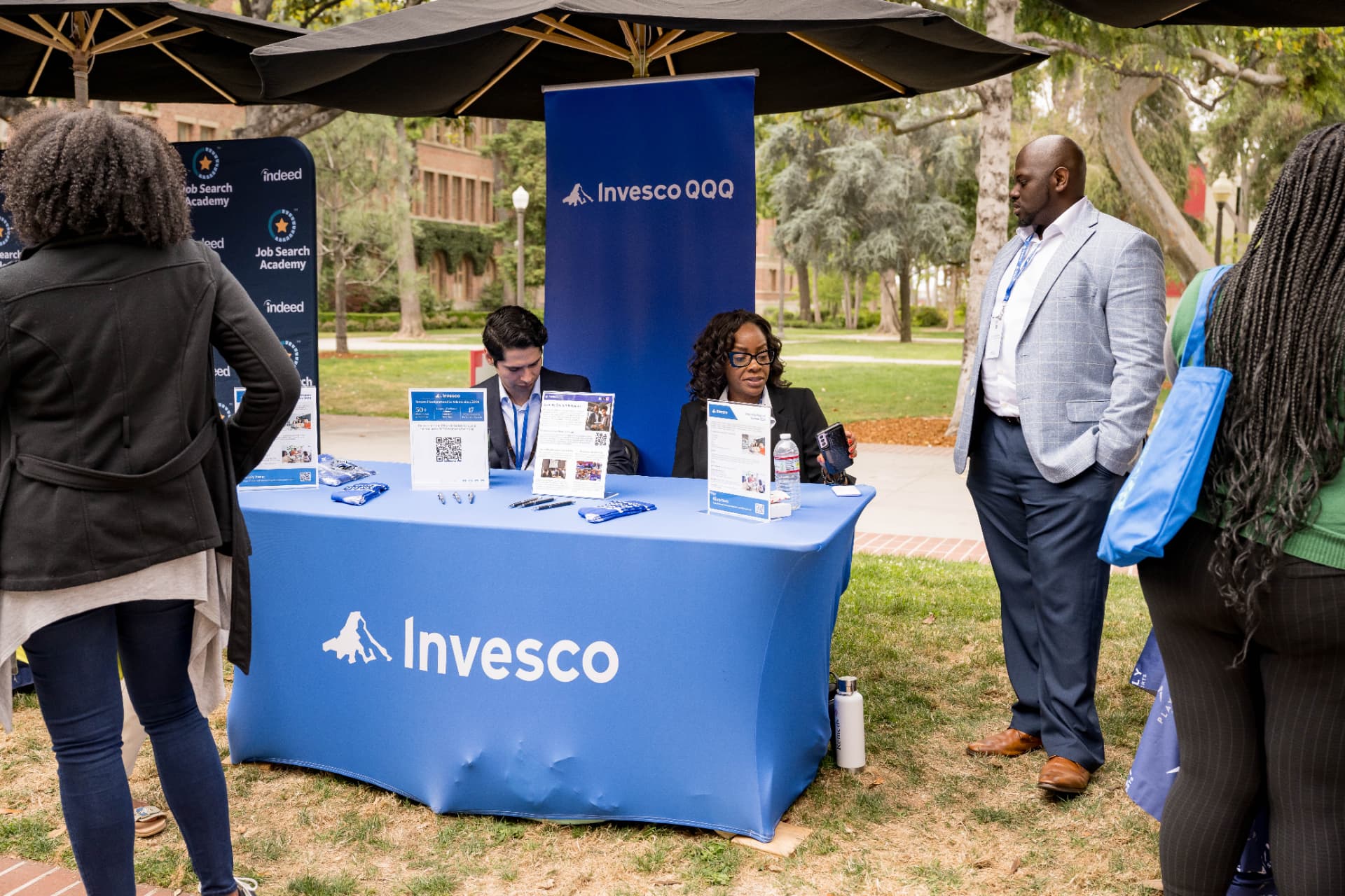 Recruiters at an Invesco QQQ career fair booth talking with attendees on a campus lawn