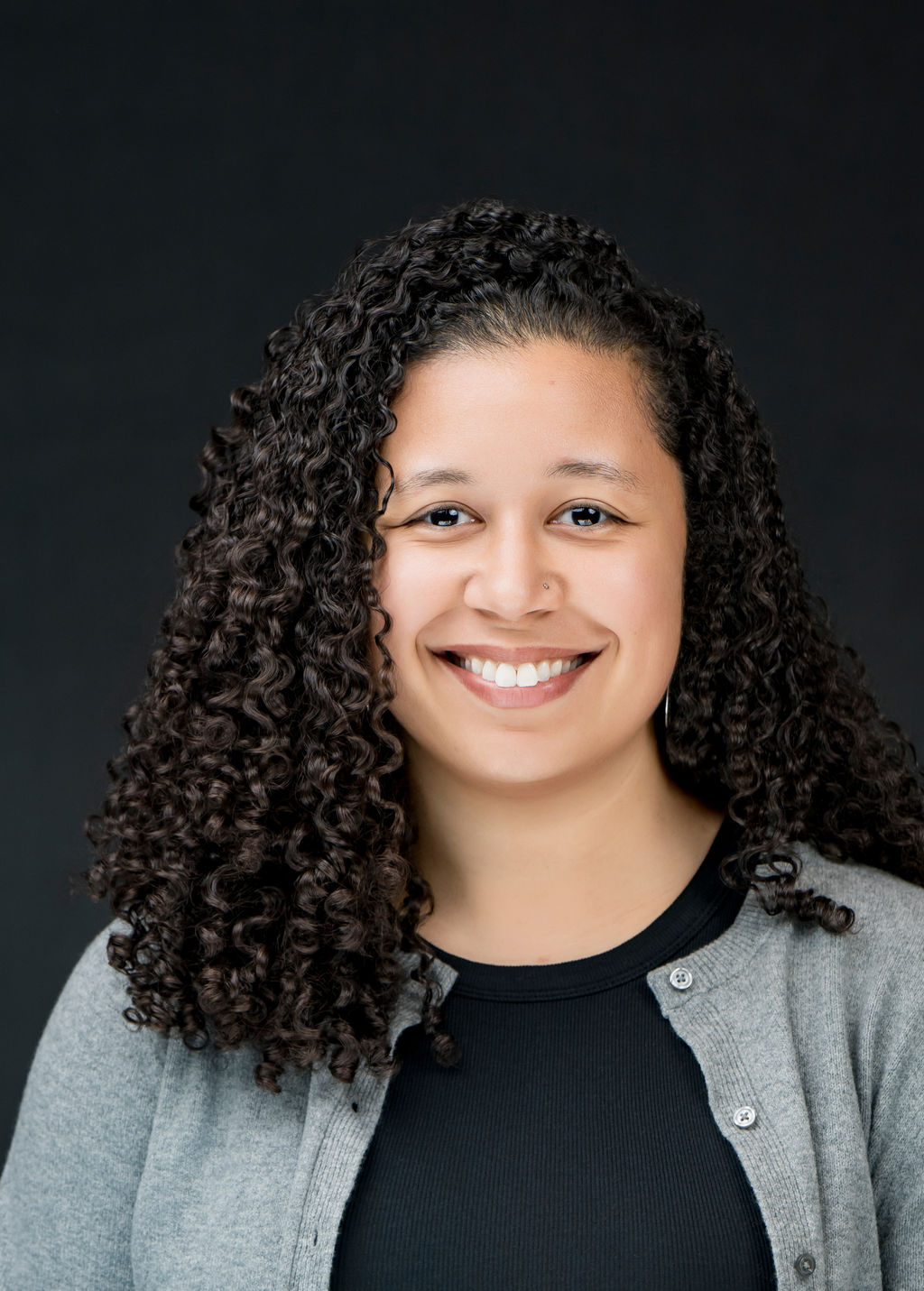 Studio headshot of a smiling woman with curly hair in a grey cardigan