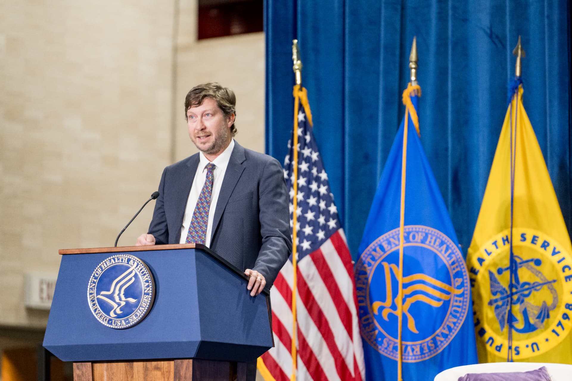 Speaker at a government podium flanked by flags