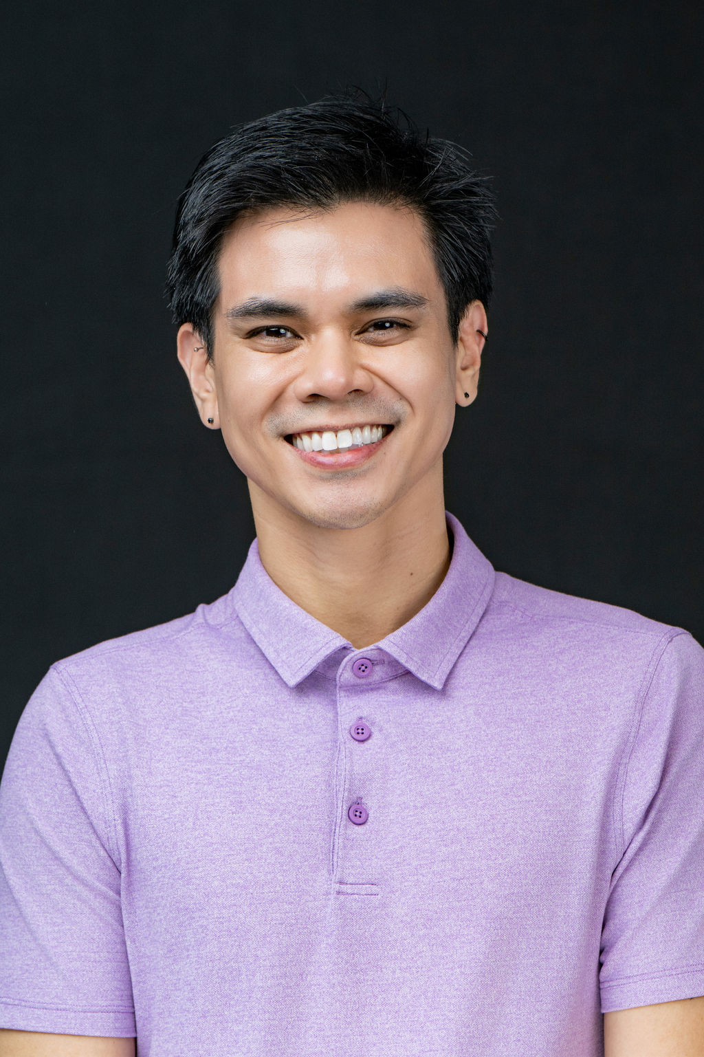 Studio headshot of a smiling man in a lavender polo shirt