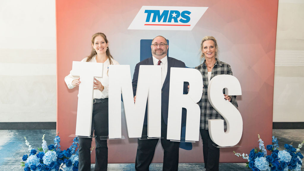 Three attendees posing with large TMRS letters at the photo backdrop