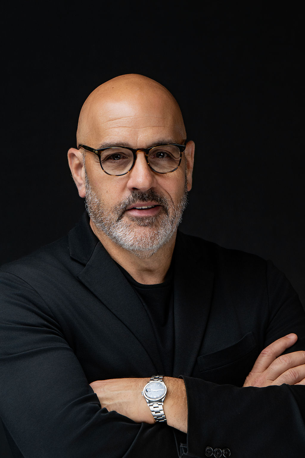 Studio portrait of a man in glasses and a black blazer with arms crossed