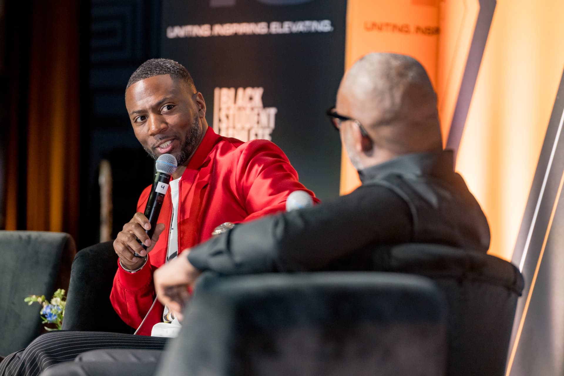 Panelist in a red jacket speaking into a microphone during a summit conversation
