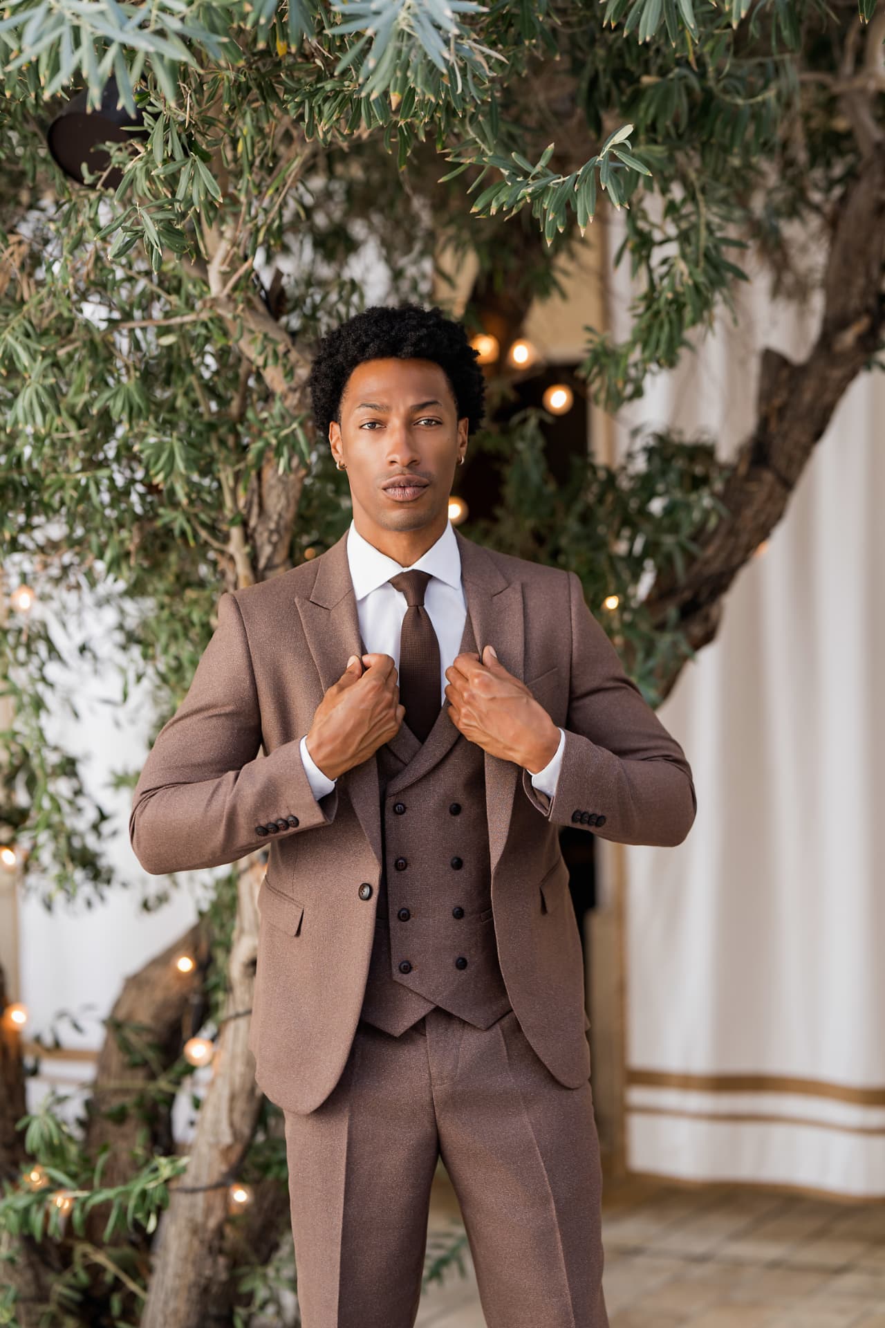 Portrait of a man in a brown three-piece suit under an olive tree