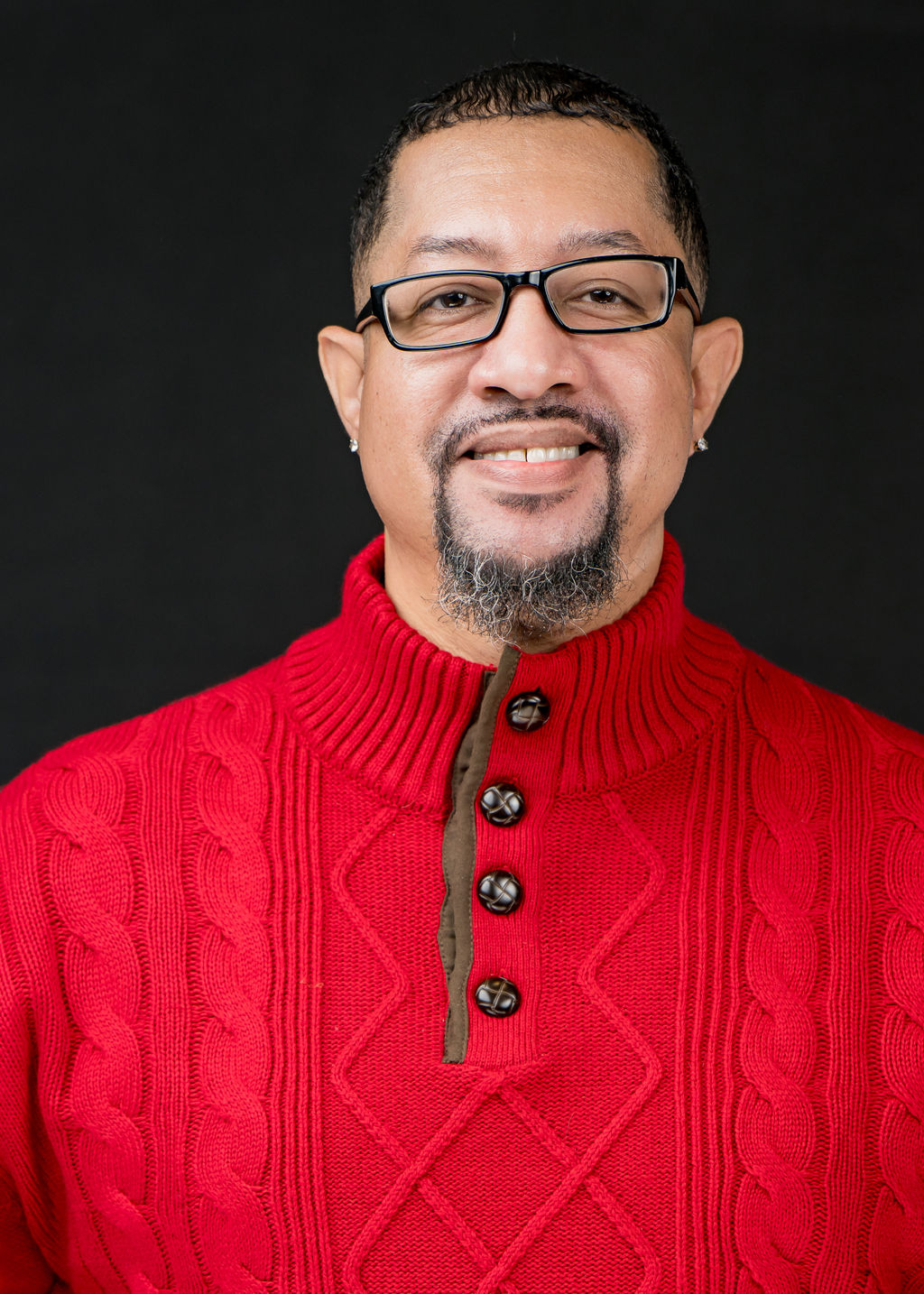 Studio headshot of a smiling man with glasses in a red cable-knit sweater