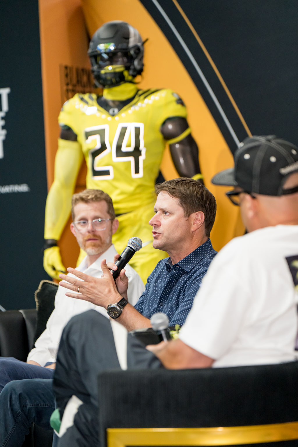 Panelists discussing on stage beside an Oregon uniform display