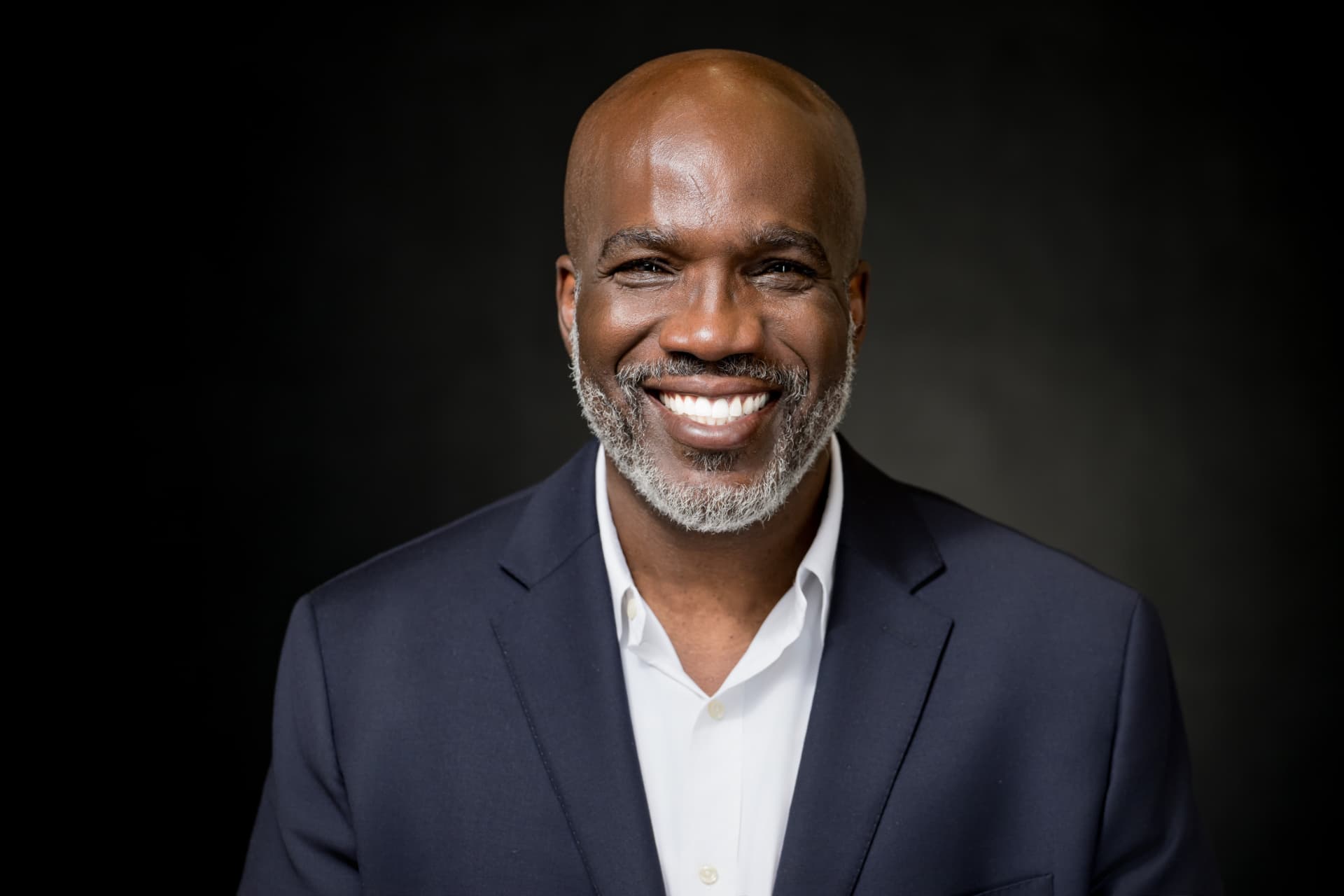 Studio headshot of a smiling man in a navy blazer and white shirt