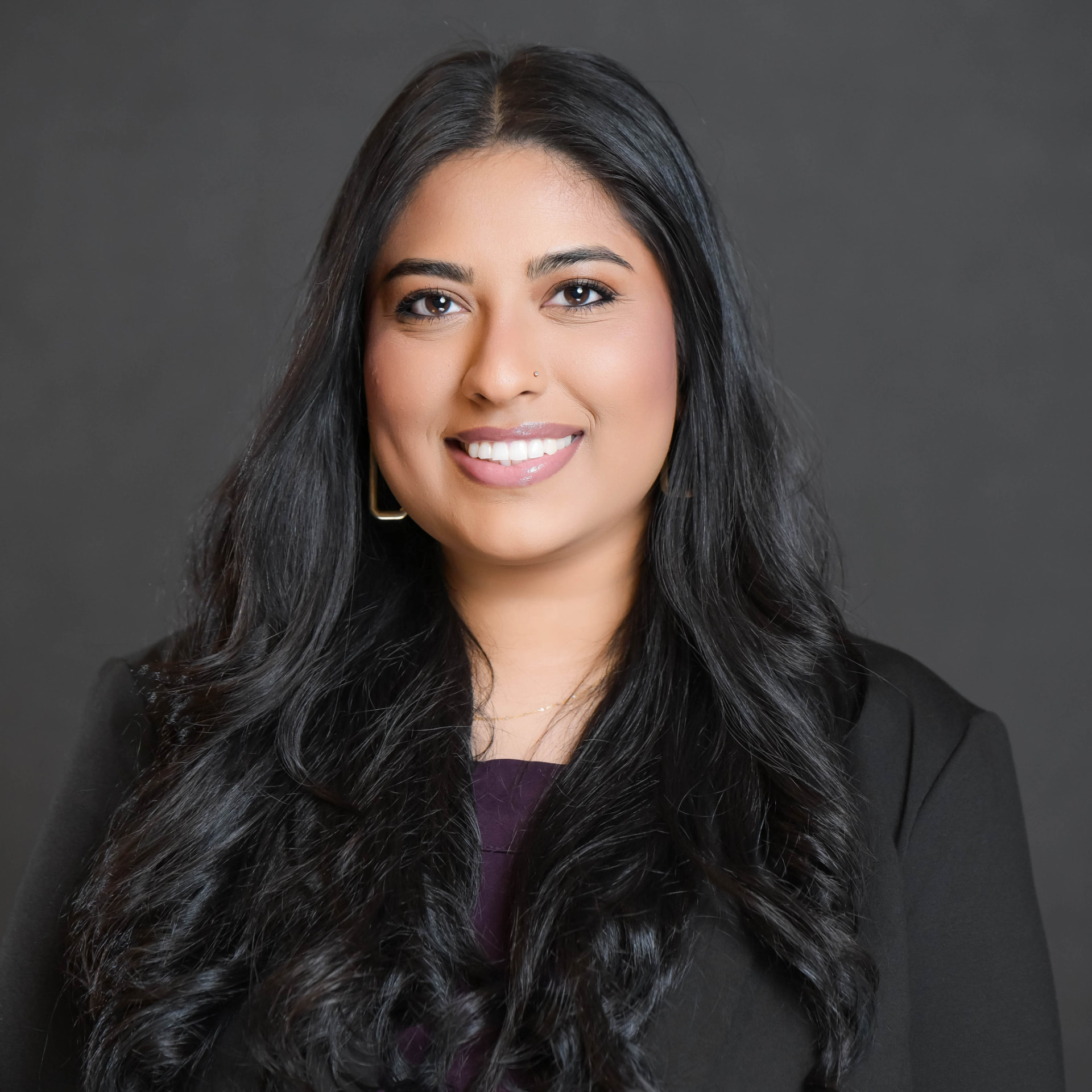Studio headshot of a professional woman with long dark hair in a charcoal blazer