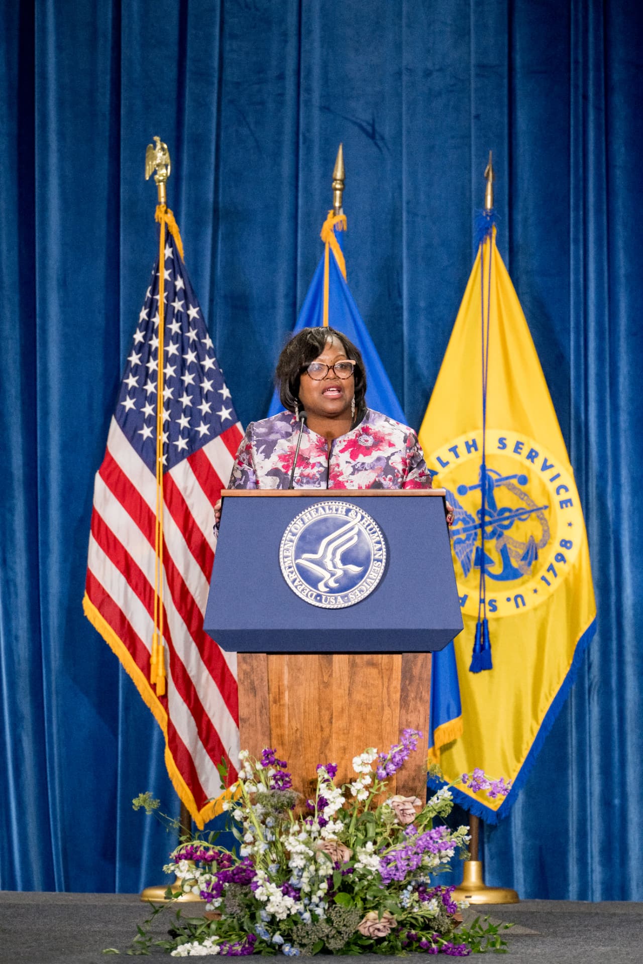 Speaker addressing guests from a wooden podium surrounded by florals and flags