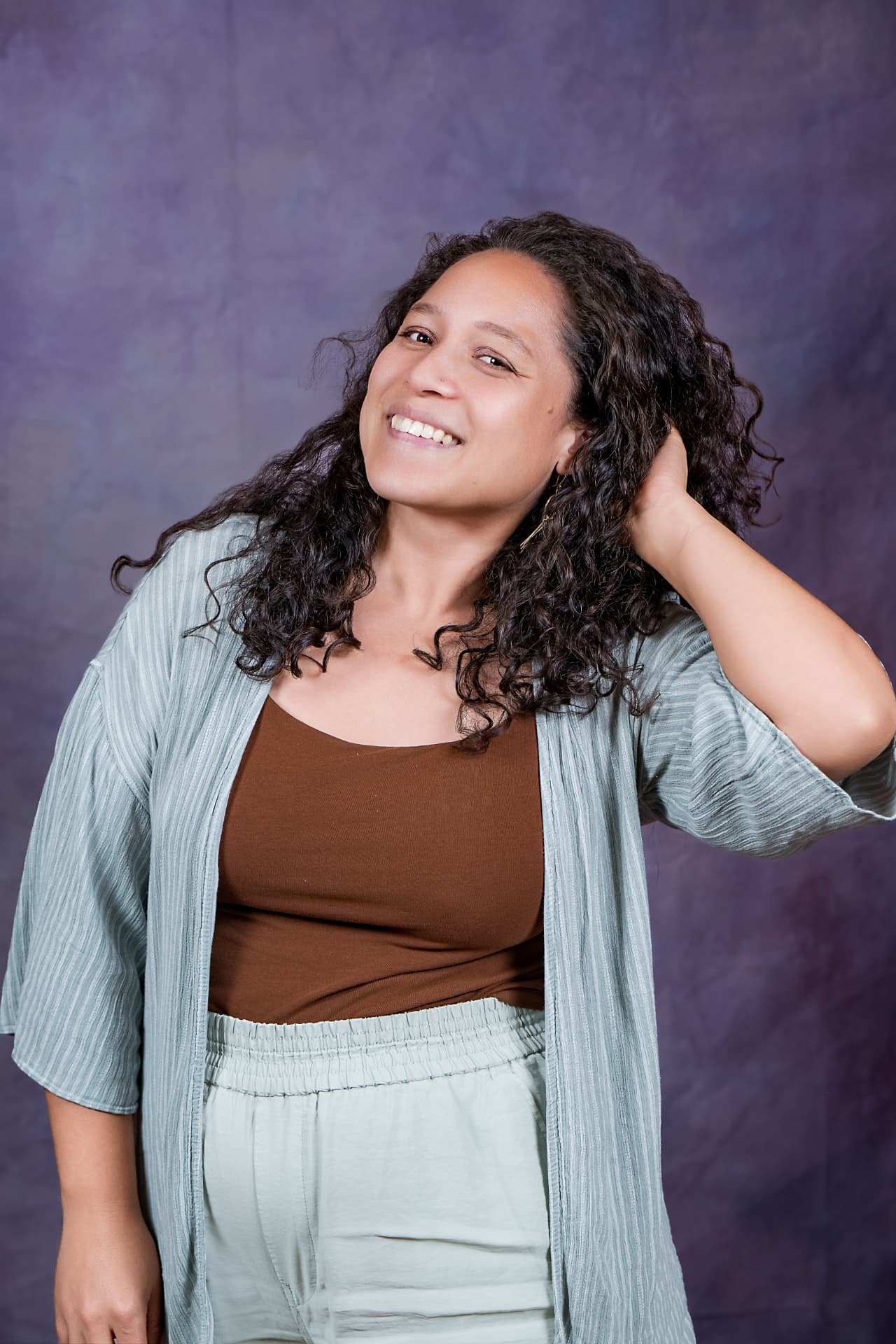 Studio portrait of a smiling woman with curly hair in a sage linen set